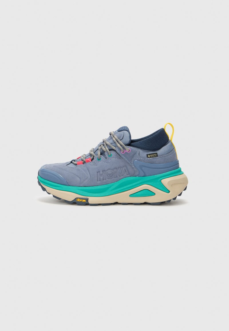 Shoe sportiv de culoare albastră deschisă, cu o talpă groasă de crem. Are accente multicolore, un material texturat la partea superioară și un tab de călcâi întărit. Logo-ul Vibram este vizibil.