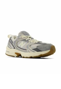 Zapatilla deportiva gris con parte superior de malla y gamuza, acentos crema, suela gruesa y banda de rodadura texturizada para tracción. Cadar y logo visibles.