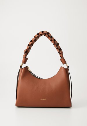 Pruun nahast käekott, millel on punutud käepide ja kuldne tõmblukk, mille keskel on etiketil "COCCINELLE" lihtsa heleda tausta ees.