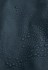 Kapky vody různých velikostí na tmavém, strukturovaném, voděodolném textilním povrchu.