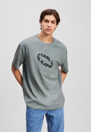 Gray cotton T-shirt with short sleeves, round neckline, and black circular text graphic on the front. Paired with light blue jeans.