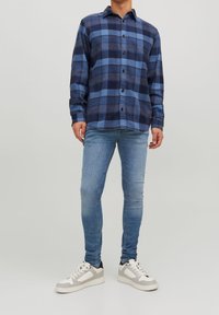 Camisa de franela a cuadros en azul y marino con diseño de botones, combinada con jeans de mezclilla azul claros y zapatillas blancas con acentos grises.
