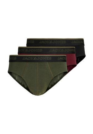 Młody mężczyzna z krótkimi blond włosami, ubrany w bordowe slipy Jack & Jones, stoi na tle jednolitego jasnego tła, zwrócony twarzą do przodu.