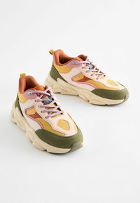 Flerfärgade sneakers med en blandning av rosa, orange, grön och gul material, med en texturerad meshöverdela och en rejäl sula.
