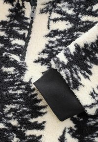 Fleece pullover med sort og creme abstrakt mønster, lynlåslukning og kontrastfarvet ribkant i sort. Blød, struktureret stof.