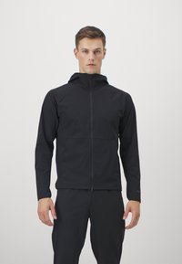 Schwarze Zip-Jacke mit Kapuze, mit Raglanärmel und Fronttaschen, aus glattem, leichtem Material. Minimalistisches Design.