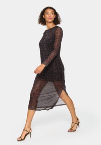 Leopard-print, sheer long-sleeve dress with a high neckline, side slits, and a loose fit, paired with strappy high heels.