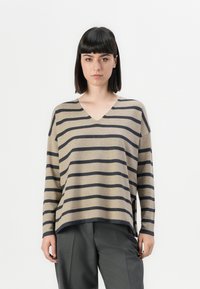 Beige stripete genser med mørk marine horisontale striper, V-hals, løs passform og senket skuldre. Kombinert med grå bukser.