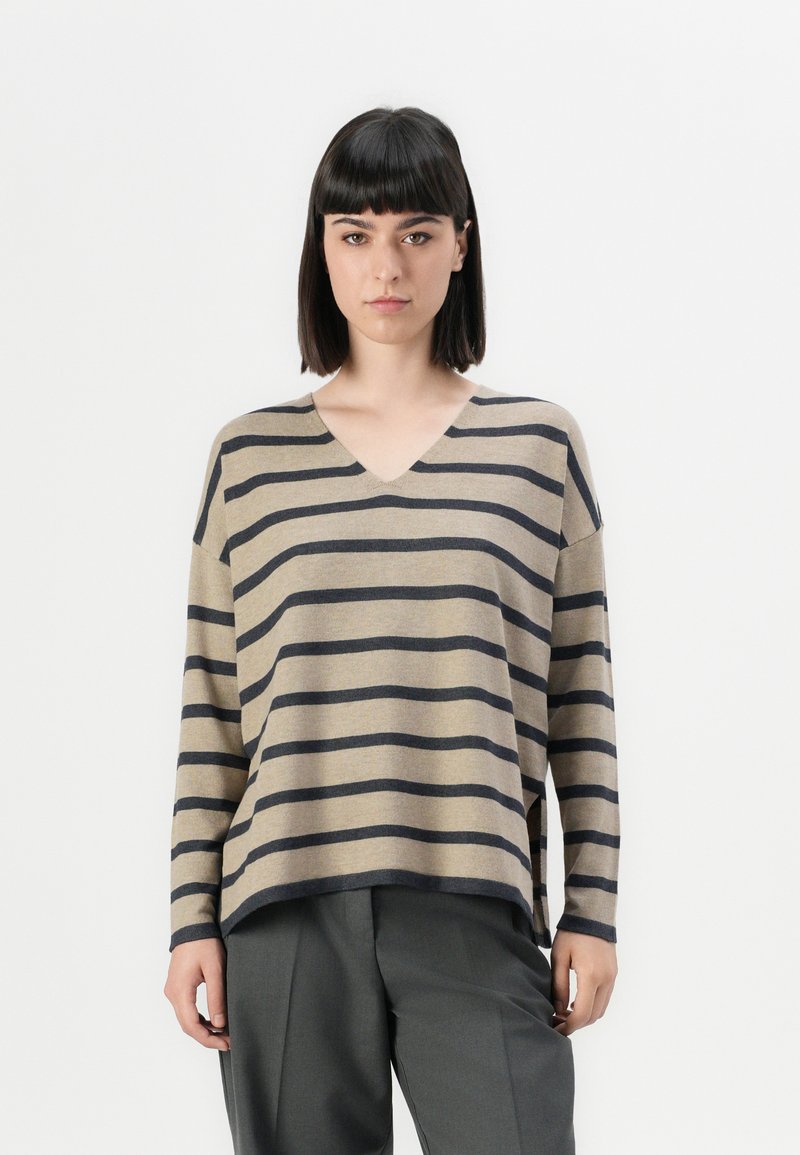 Beige stripete genser med mørk marine horisontale striper, V-hals, løs passform og senket skuldre. Kombinert med grå bukser.
