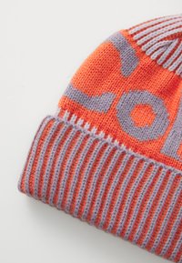 Gorro de malha laranja com padrão geométrico em roxo claro. Possui uma aba canelada e uma textura suave.