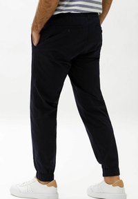 Marina joggerbyxor med elastiska muddar, sidofickor och bakfickor, samt en avslappnad passform, i kombination med vita sneakers med bruna detaljer.