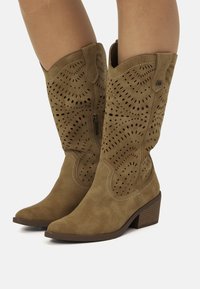 Botas de cowboy de ante marrón con diseño perforado, punta afilada, tacón bajo apilado y costuras en contraste. Cierre de cremallera en el lateral.