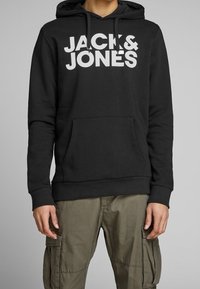 Schwarzer Hoodie aus Baumwollmischung mit einer frontalen Kängurutasche und großem, weißem Drucklogo "JACK & JONES" auf der Brust.