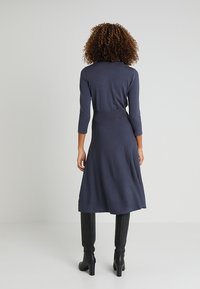 Robe bleu marine à manches longues avec une taille ajustée et une jupe évasée. Fabriquée en tissu doux, elle présente une texture lisse et des coutures subtiles.