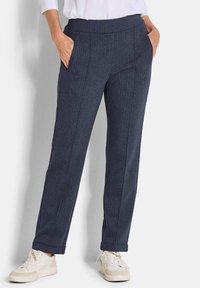 Donkerblauwe broek in een visgraatpatroon met een rechte snit, voorzien van zijzakken en een opgerolde zoom, gedragen met witte sneakers.