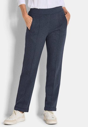 Donkerblauwe broek in een visgraatpatroon met een rechte snit, voorzien van zijzakken en een opgerolde zoom, gedragen met witte sneakers.