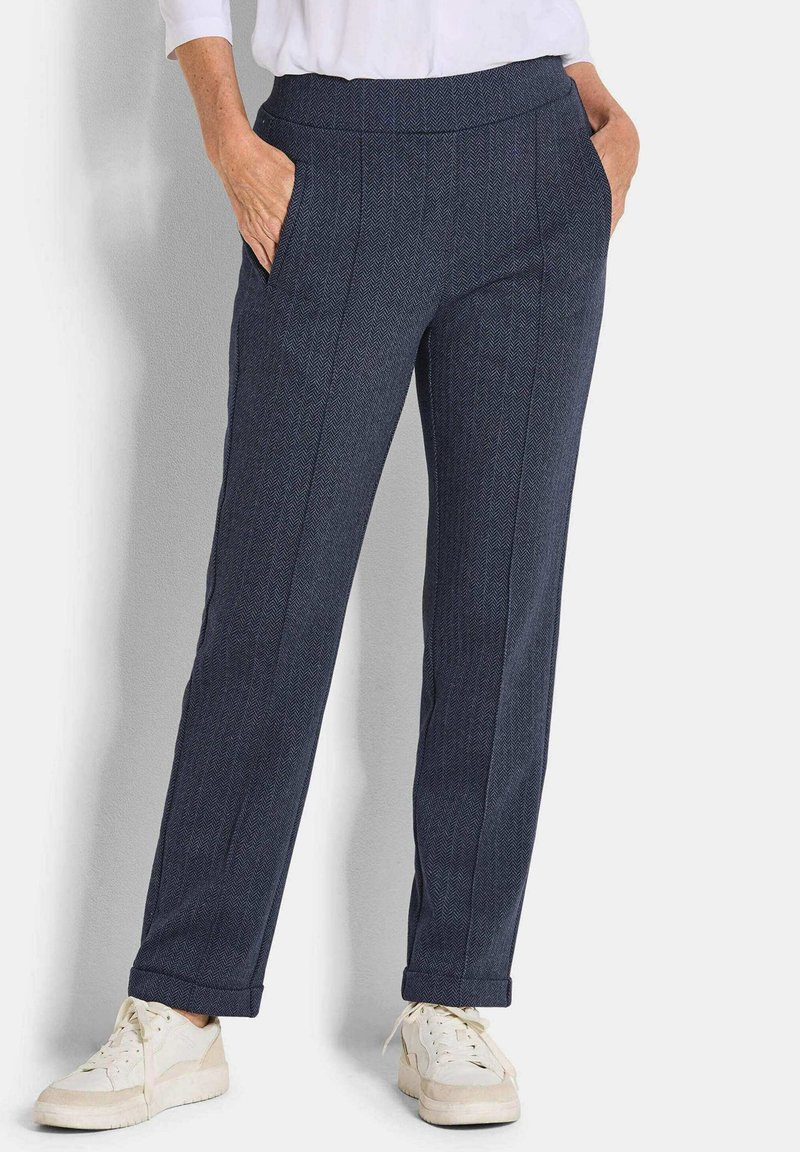 Donkerblauwe broek in een visgraatpatroon met een rechte snit, voorzien van zijzakken en een opgerolde zoom, gedragen met witte sneakers.