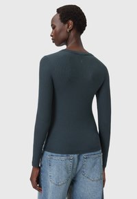 Maglia a maniche lunghe a coste verde scuro con scollatura rotonda e design aderente, abbinata a jeans in denim azzurri con tasche posteriori.