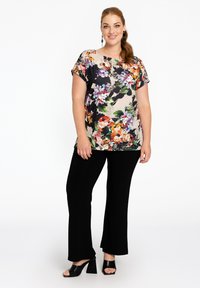 Blumenmuster Kurzarmoberteil mit bunten Mustern auf einem hellen Hintergrund, kombiniert mit schwarzen Schlaghosen und klobigen Absatzsandalen.