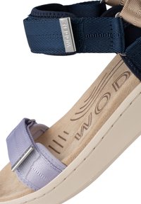 Sandaler med ett lilafärgat band och ett justerbart marinblått band, med en vadderad beige fotbädd med logotypavtryck och en tjock vit sula.