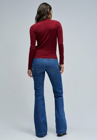 Pull ajusté maroon à manches longues associé à un jean évasé bleu. Le jean présente un design classique de poches et un léger délavage sur les cuisses.