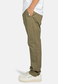 Khaki-Chinos im geraden Schnitt, aus Baumwolle mit glatter Textur. Mit seitlichen Taschen und kombiniert mit weißen Sneakern.