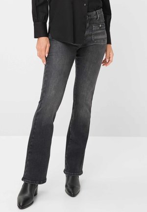 Jeans svasati di un grigio scuro con una texture liscia, tasche frontali e dettagli di cucitura sottili, abbinati a un top nero e stivali alla caviglia.