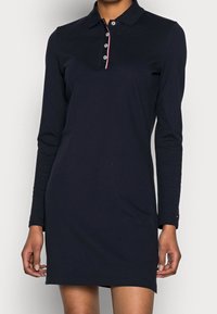 Marinblå långärmad polo klänning med krage, treknappsstängning och röd kant vid halslinningen. Tillverkad av mjukt, slätt bomullstyg.