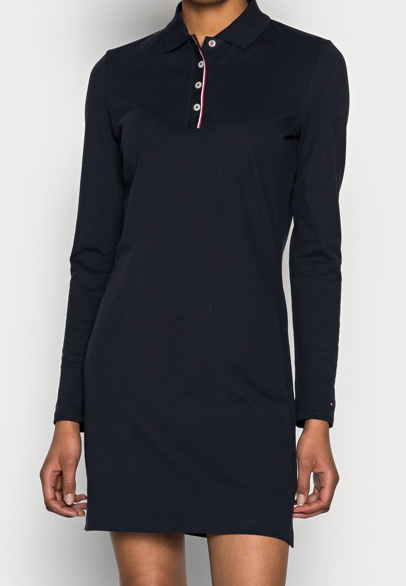 Marinblå långärmad polo klänning med krage, treknappsstängning och röd kant vid halslinningen. Tillverkad av mjukt, slätt bomullstyg.