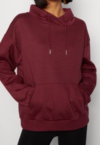 Sudadera con capucha burdeos, mezcla de algodón, corte oversize, bolsillo canguro, cordones con extremos de metal, puños y dobladillo acanalados.