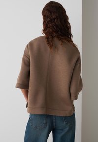 Un sweatshirt brun surdimensionné avec des manches courtes, une texture douce et un détail de couture à l'arrière, associé à un jean en denim bleu.