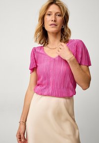 Kortærmet lyserød bluse med et struktureret, plisseret design og V-hals, parret med en flydende cremefarvet nederdel. Glat, let stof.