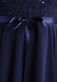 Robe marine avec un corsage en dentelle ornée de sequins, dotée d'une ceinture en satin et d'une jupe fluide et texturée.