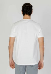 Camiseta de algodón blanca con mangas cortas, escote redondo y una textura suave. La vista desde atrás muestra un corte relajado y un diseño minimalista.