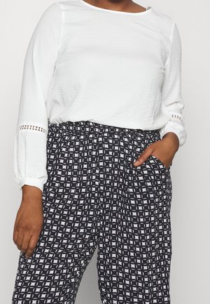 Maglietta bianca a maniche lunghe con tessuto testurizzato e dettagli in pizzo, abbinata a pantaloni elasticizzati bianchi e neri con motivo e tasche laterali.