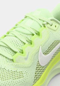 Zapatilla atlética de malla verde con una superficie texturizada, acentos reflectantes y lengua ligeramente acolchada con detalles en neón amarillo en contraste.