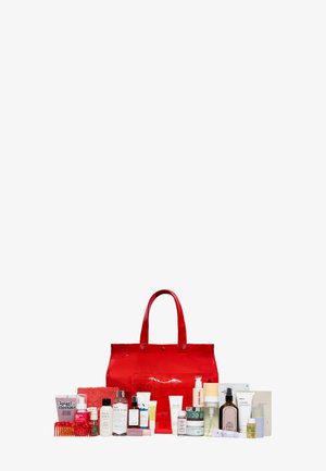 Sac fourre-tout transparent rouge avec une gamme de produits de soin de la peau et de beauté disposés devant sur un fond blanc.