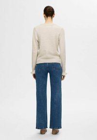 Pull beige clair à manches longues, cintré à la taille, associé à un jean en denim bleu à jambes larges avec poches arrière. Texture lisse.