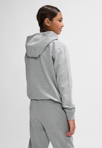 Grauer Hoodie aus weichem Stoff, mit großer Kapuze und gerippten Bündchen, kombiniert mit passenden grauen Jogginghosen.