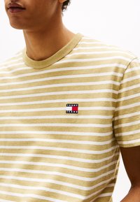 Kollane ja valge triibuline T-särk ümarate kaelustega, vasakul küljel on väike broderitud "TOMMY JEANS" logo. Pehme kangastekstuuri.