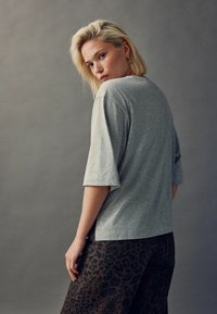 Szary krótki rękaw t-shirt o luźnym kroju, w zestawieniu z brązowymi spodniami w cętki z motywem lamparta. Materiał wydaje się miękki i swobodny.