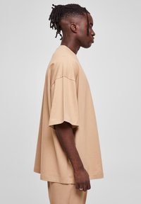 Beige oversized T-shirt med korte ærmer, lavet af blødt stof. Har en rund halsudskæring og en afslappet pasform, detaljeret med enkle stikninger.