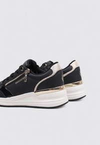 Scarpe sportive nere con accenti dorati, dettaglio con cerniera e retro testurizzato, caratterizzate da una suola bianca imbottita e un design elegante.
