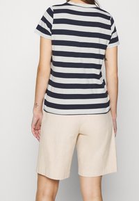 Námorný a krémový pruhovaný tričko s krátkým rukávem a kulatým výstřihem, spárované s béžovými šortkami. Měkký, lehký materiál.