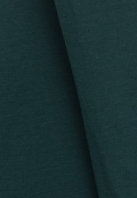 Mörkgrön tyg med fin ribbad textur och mjuka veck som skapar skuggor och djup.