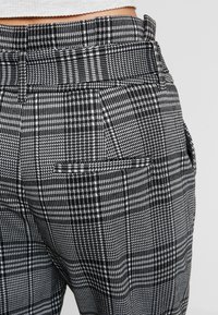 Černobílé kostkované kalhoty s vysokým pasem, které mají hladkou texturu, boční kapsu a pečlivé švy.