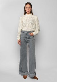 Spitzenoberteil in Off-White mit hohem Kragen und Puffärmeln, kombiniert mit weit geschnittenen grauen Jeans aus Denim mit umgeschlagenen Säumen und Gürtelschlaufen.