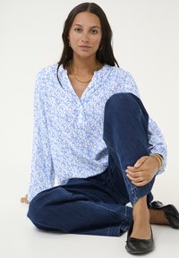 Chemise à manches longues bleu et blanche à motifs avec un col, associée à un pantalon en denim bleu foncé et des chaussures plates noires. Style décontracté, coupe confortable.