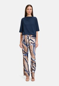 Granatowa bluzka o fakturze i luźnym kroju z rękawami ¾, zestawiona z szerokimi spodniami we wzory w odcieniach brązu, niebieskiego i kremowego.