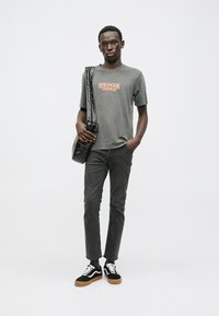 Szara koszulka z napisem "STRANGER THINGS", czarna torba na ramię, szare spodnie oraz czarne trampki z białymi akcentami i gumową podeszwą.